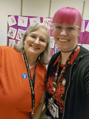 Two lab professionals, one in an orange shirt and one with pink hair, celebrating their union victory!